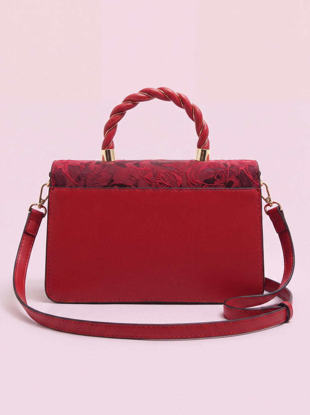 Red Monaco handbag shown from the back, featuring a smooth red leather panel, floral-patterned fabric along the upper edge, braided top handle with gold-tone hardware, and a detachable shoulder strap on a soft pink background.