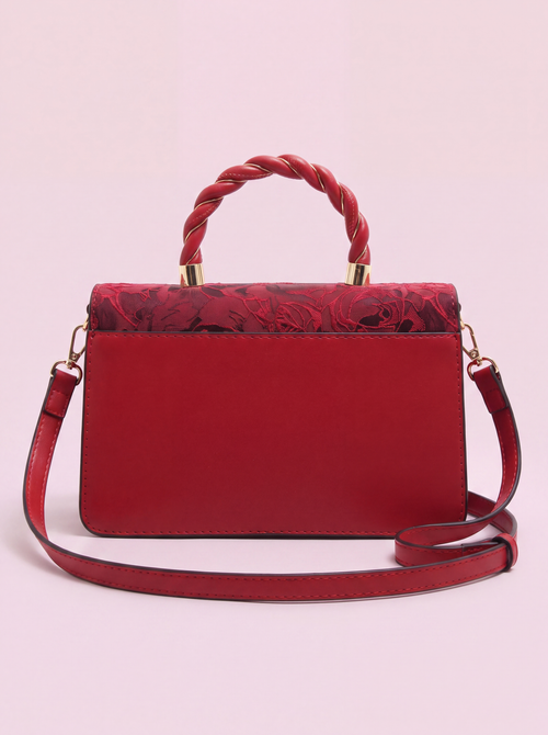 Red Monaco handbag shown from the back, featuring a smooth red leather panel, floral-patterned fabric along the upper edge, braided top handle with gold-tone hardware, and a detachable shoulder strap on a soft pink background.
